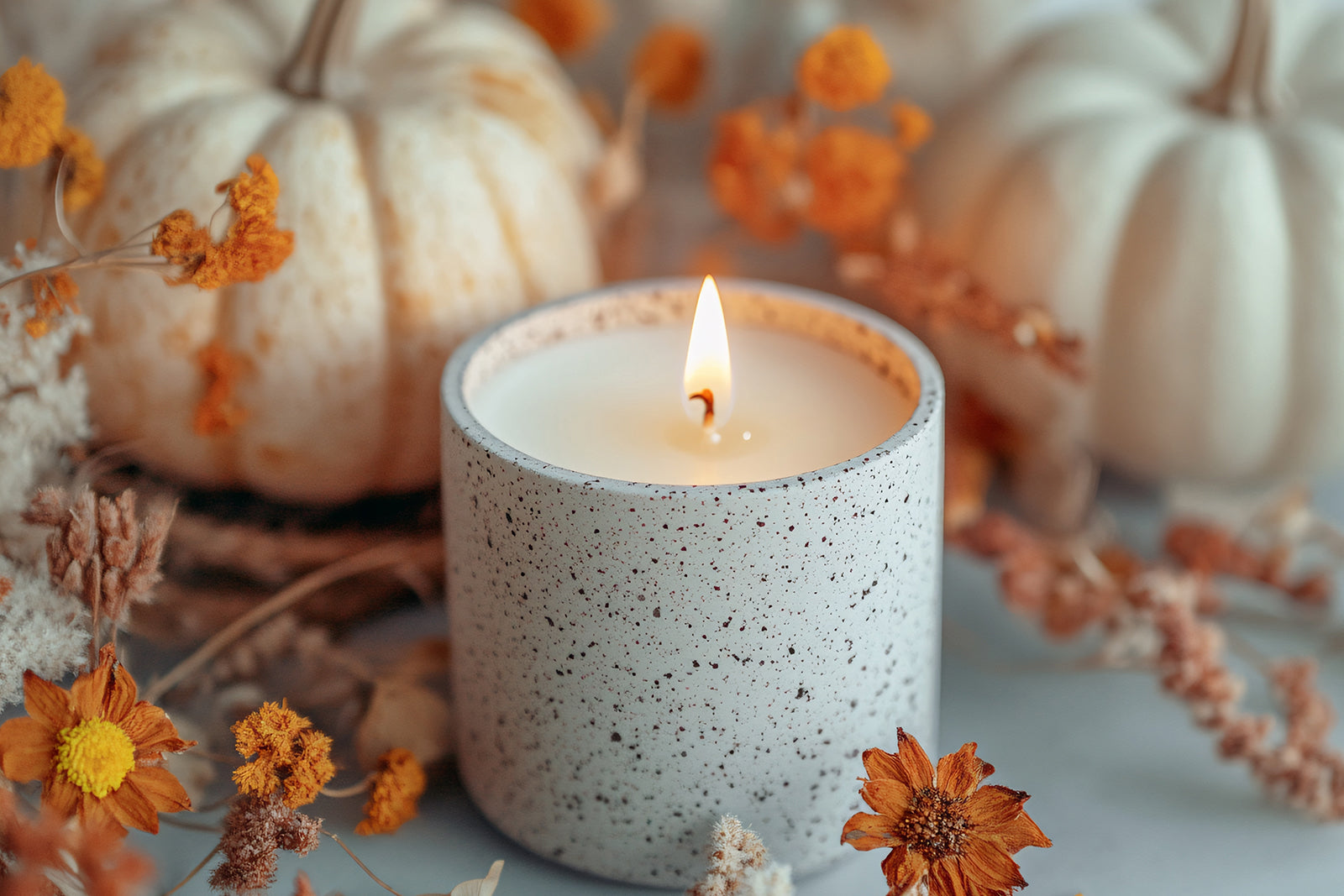 luxury fall candles worth the splurge - a candle in stone container with pumpkins and faux fall flowers
