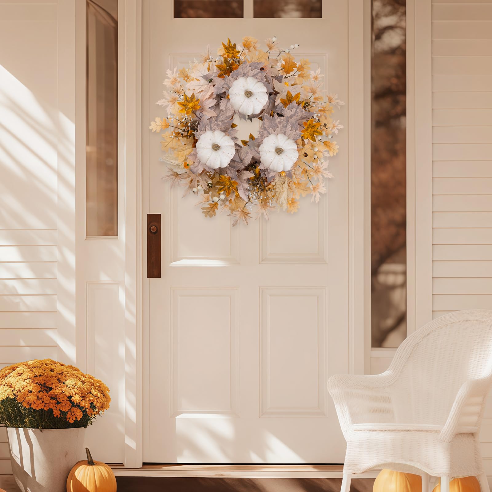 Decorative wreath on a front door with pumpkins and flowers on the ground.