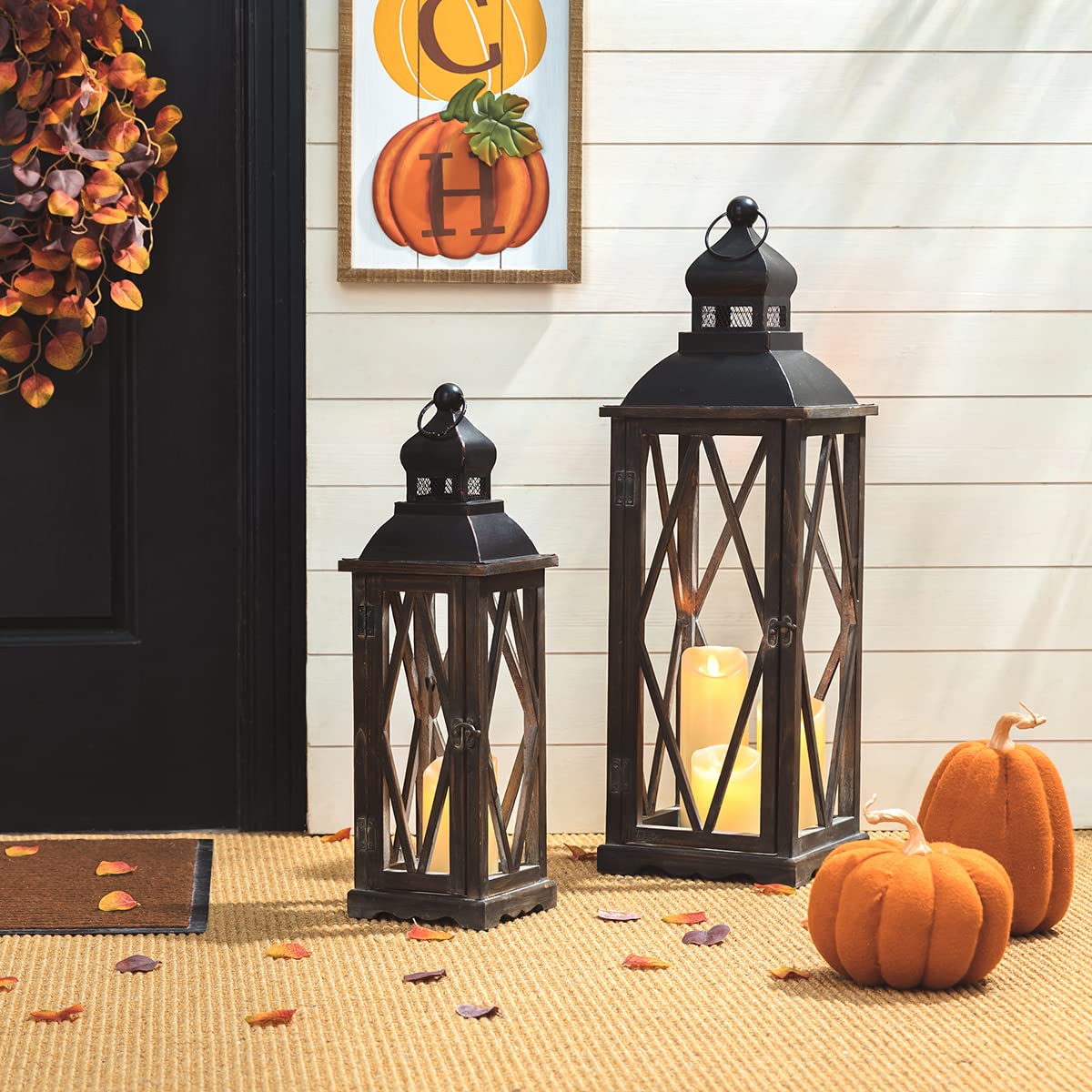 Decorative lanterns with candles, pumpkins, and a wreath on a door with a pumpkin-themed sign in the background.
