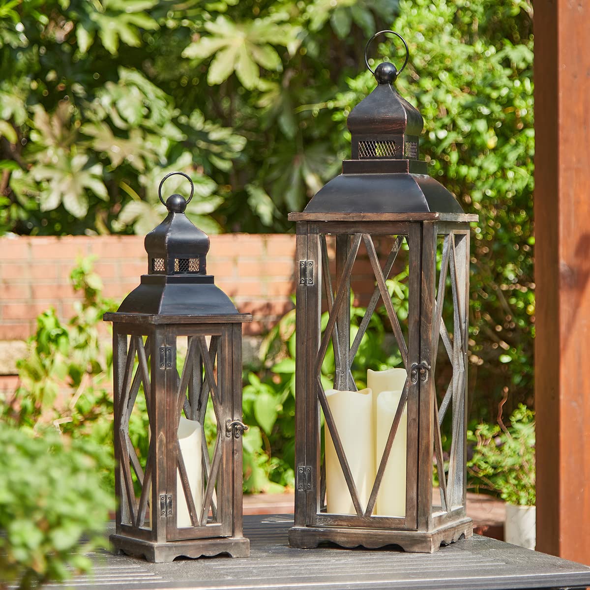 Two wooden lanterns with candles inside on a wooden surface outdoors.