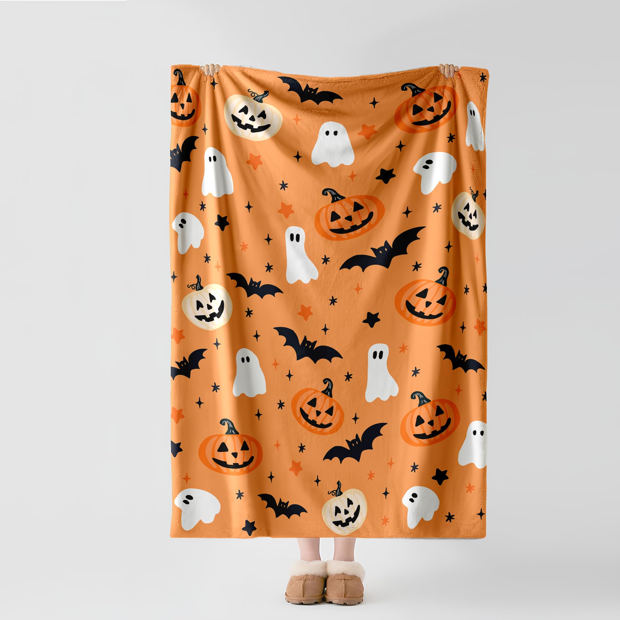 Person holding up an orange blanket with pumpkins, ghosts, and bats.