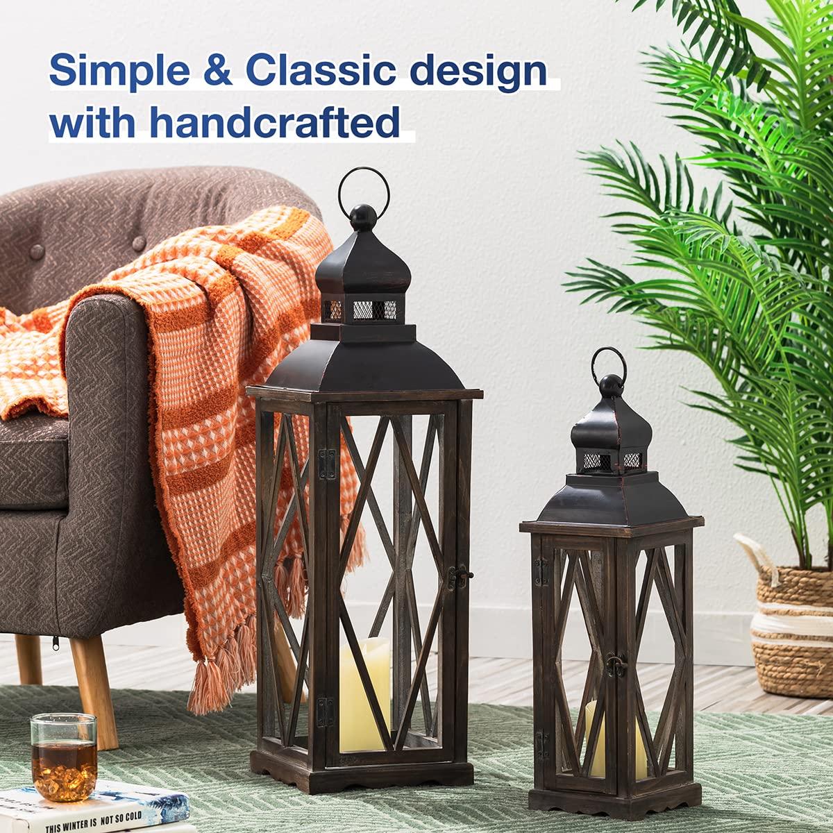 Two dark metal lanterns on a green rug with a gray chair and orange blanket in the background.