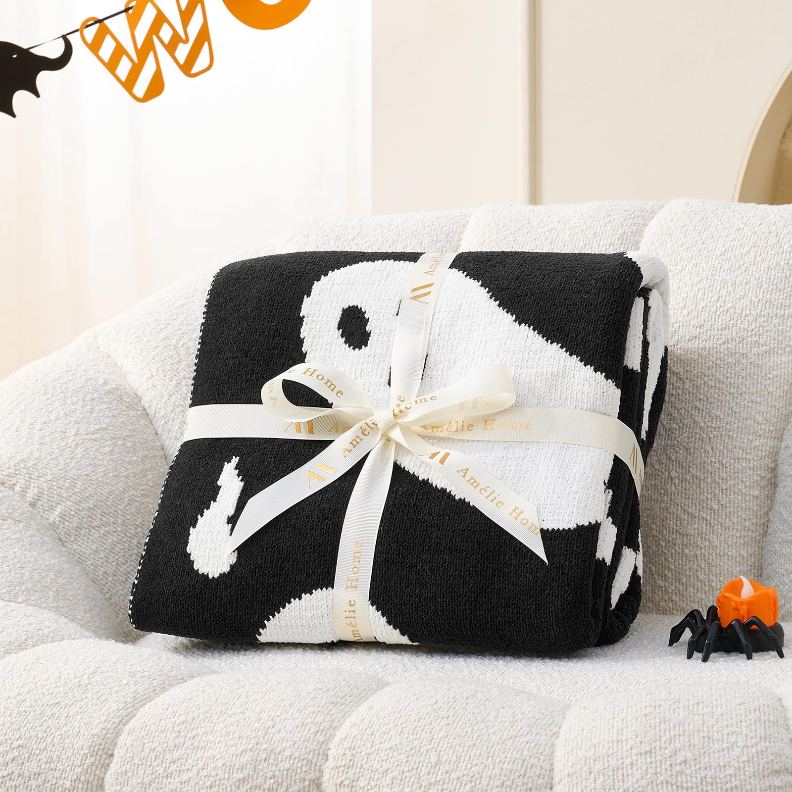 Black and white patterned blanket with a bow on a white couch, Halloween decorations in the background.