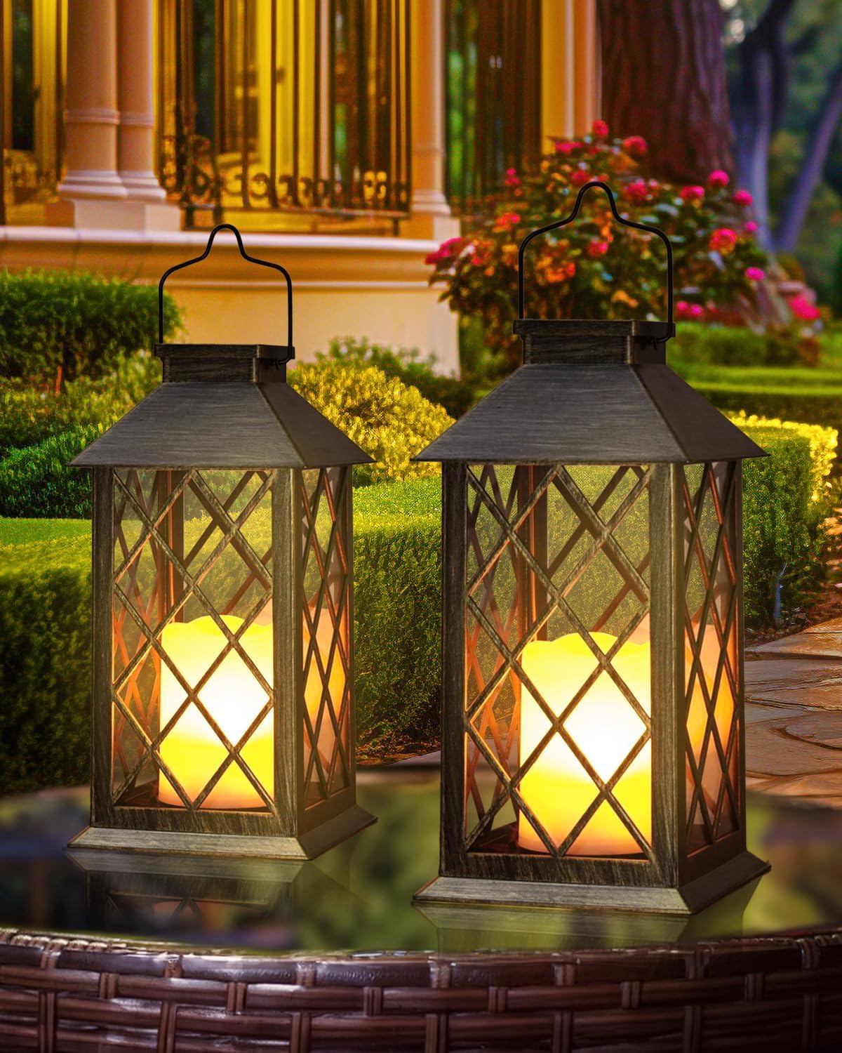 Two lit outdoor lanterns on a patio with garden and house in the background