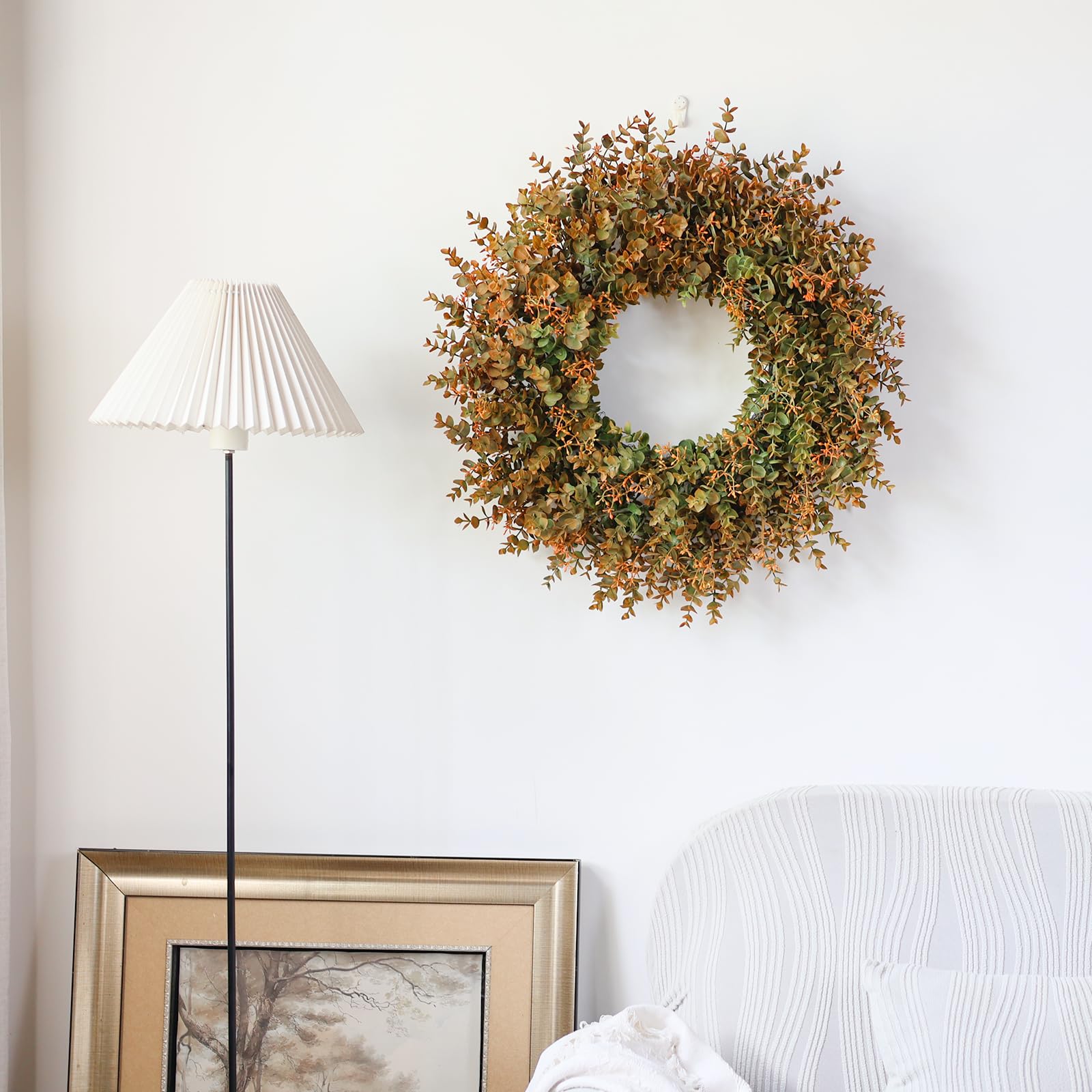 Decorative fall wreath on a wall next to a lamp and framed picture
