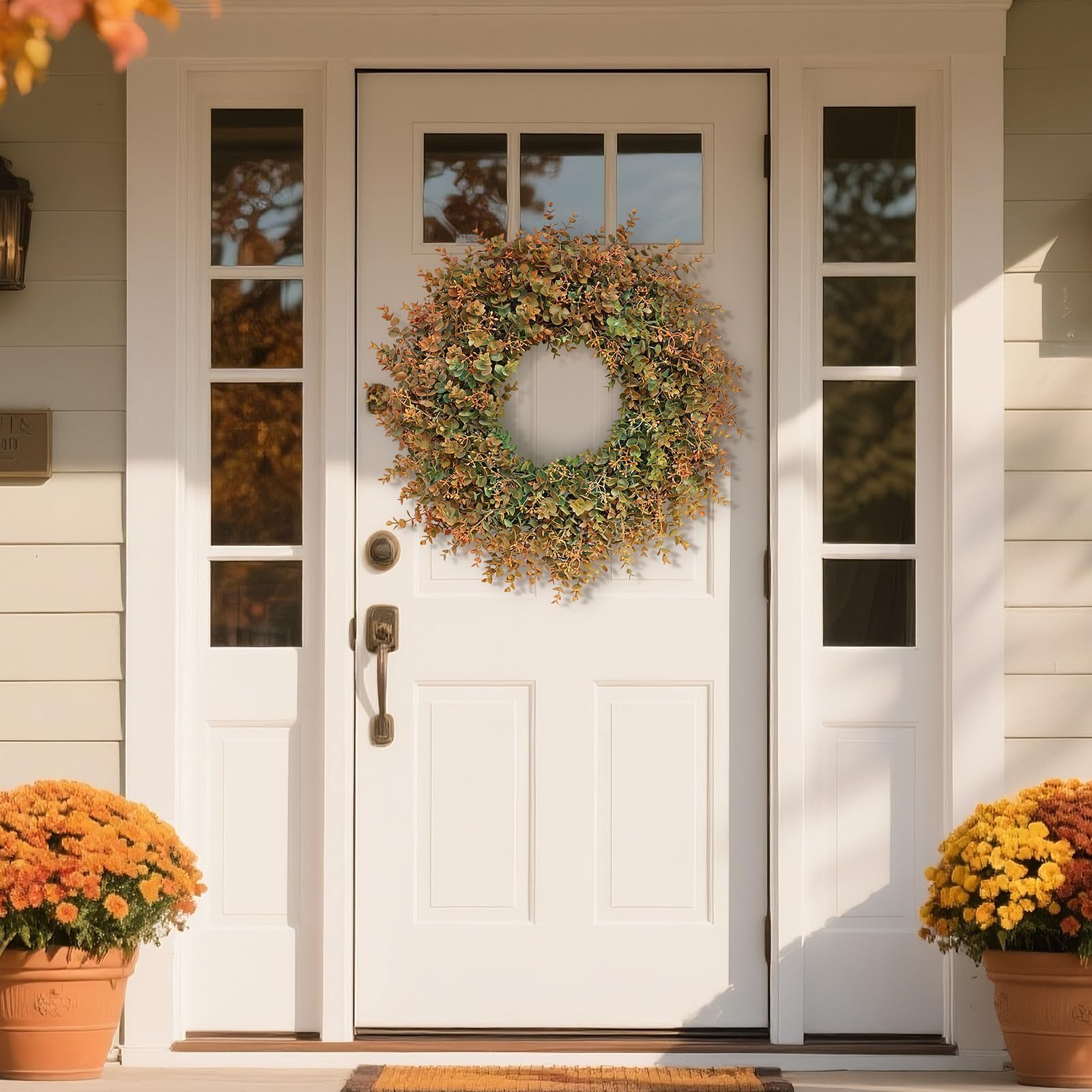 White front door with a decorative autumn wreath. Accented by potted flowers on a sunny day.