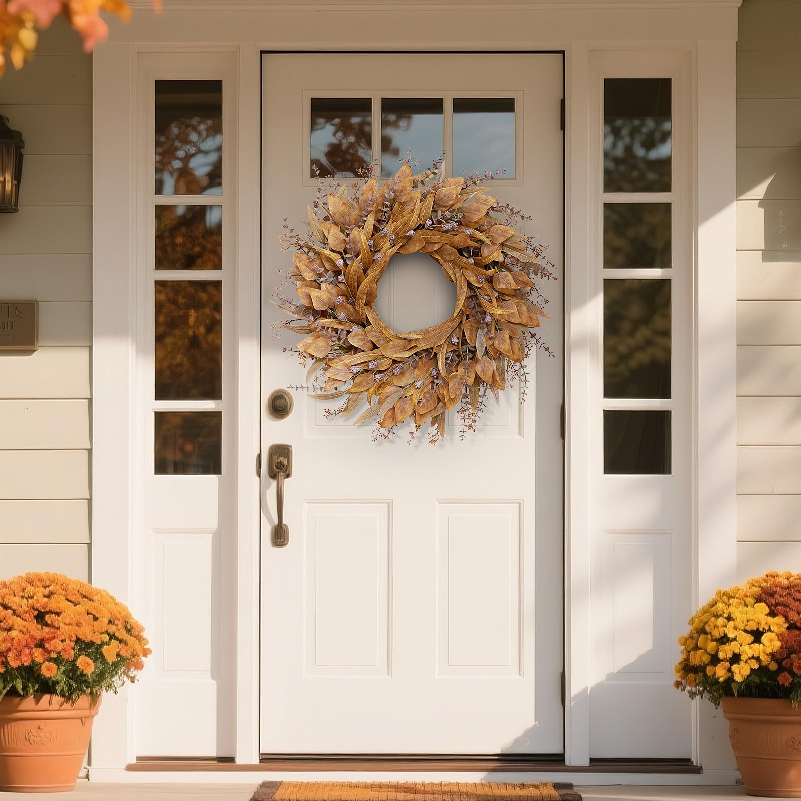 White front door with a decorative fall wreath, with by two potted plants on a porch.