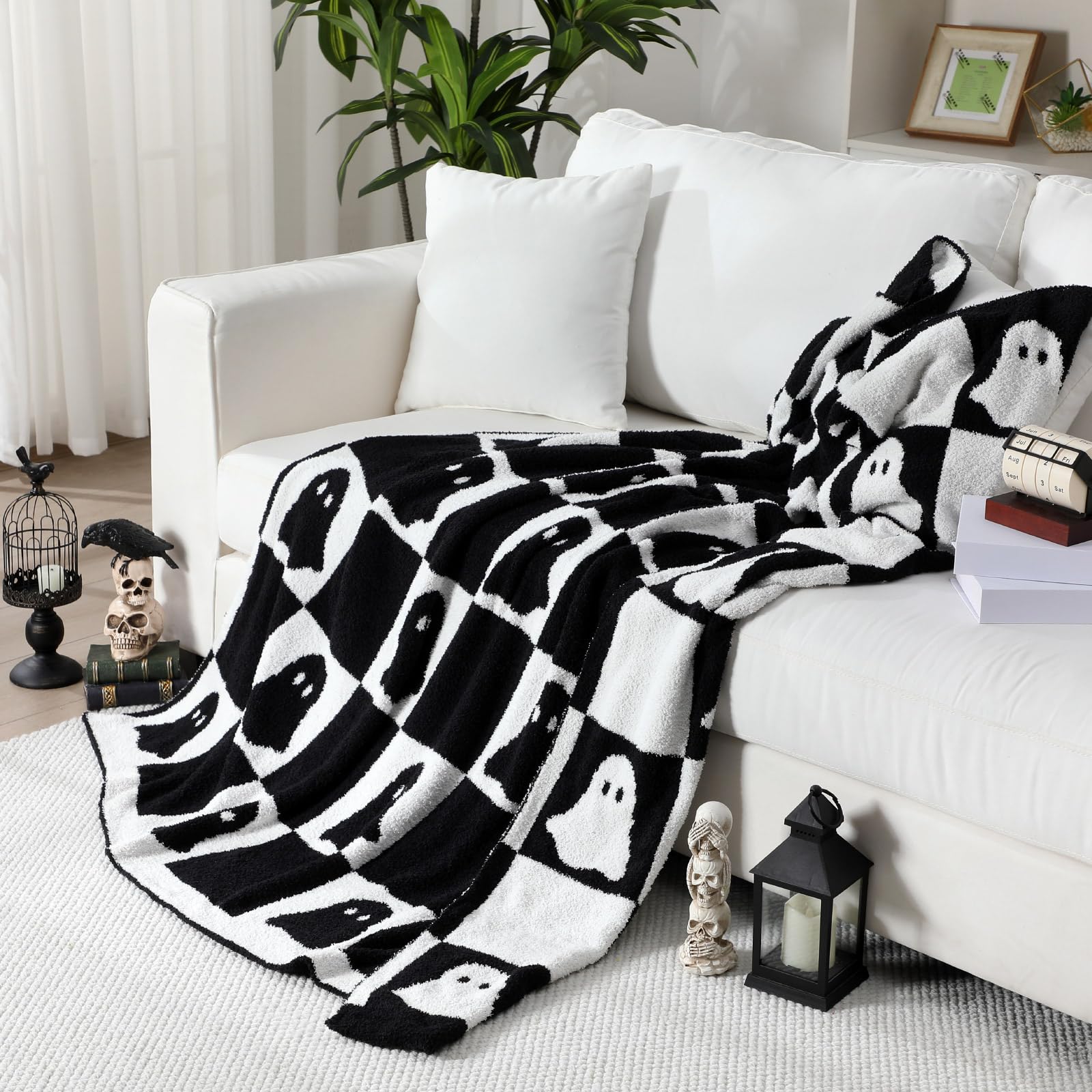Black and white ghost patterned Halloween blanket draped over a white sofa in a living room.