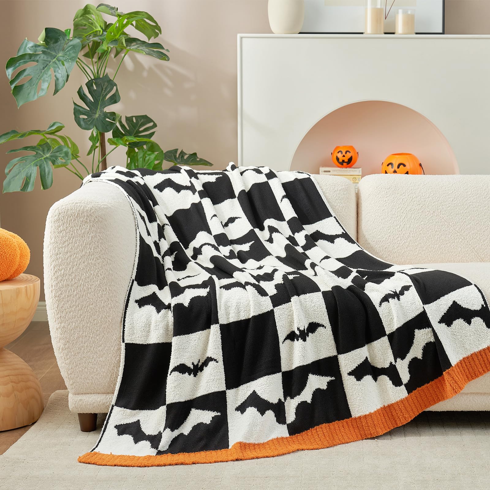 Halloween-themed blanket with bat patterns draped over a white armchair in a room with Halloween decorations.